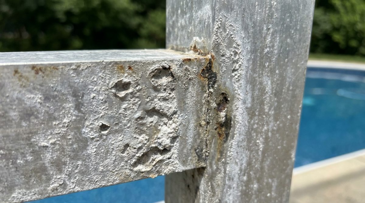 Close-up of pitting and chalky residue on a poorly specified metal pool enclosure frame, showing surface degradation from salt and UV exposure